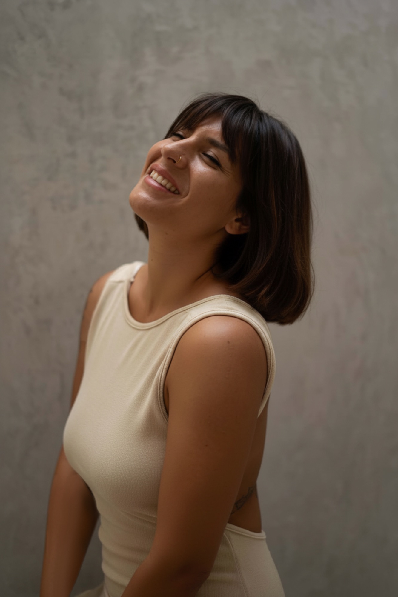 Emanuela smiling, head tilted back, against a soft grey wall